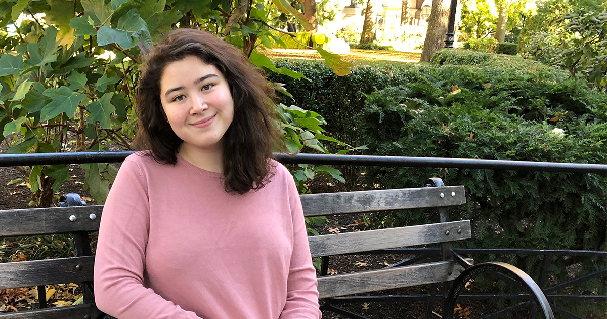 Erin Yun, author of the Pippa Park series, is sitting outside on a wooden bench and smiling. 