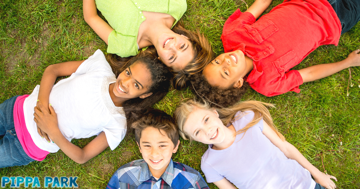 Five kids (three girls and two boys) are laying on grass in a circle looking up and smiling. 