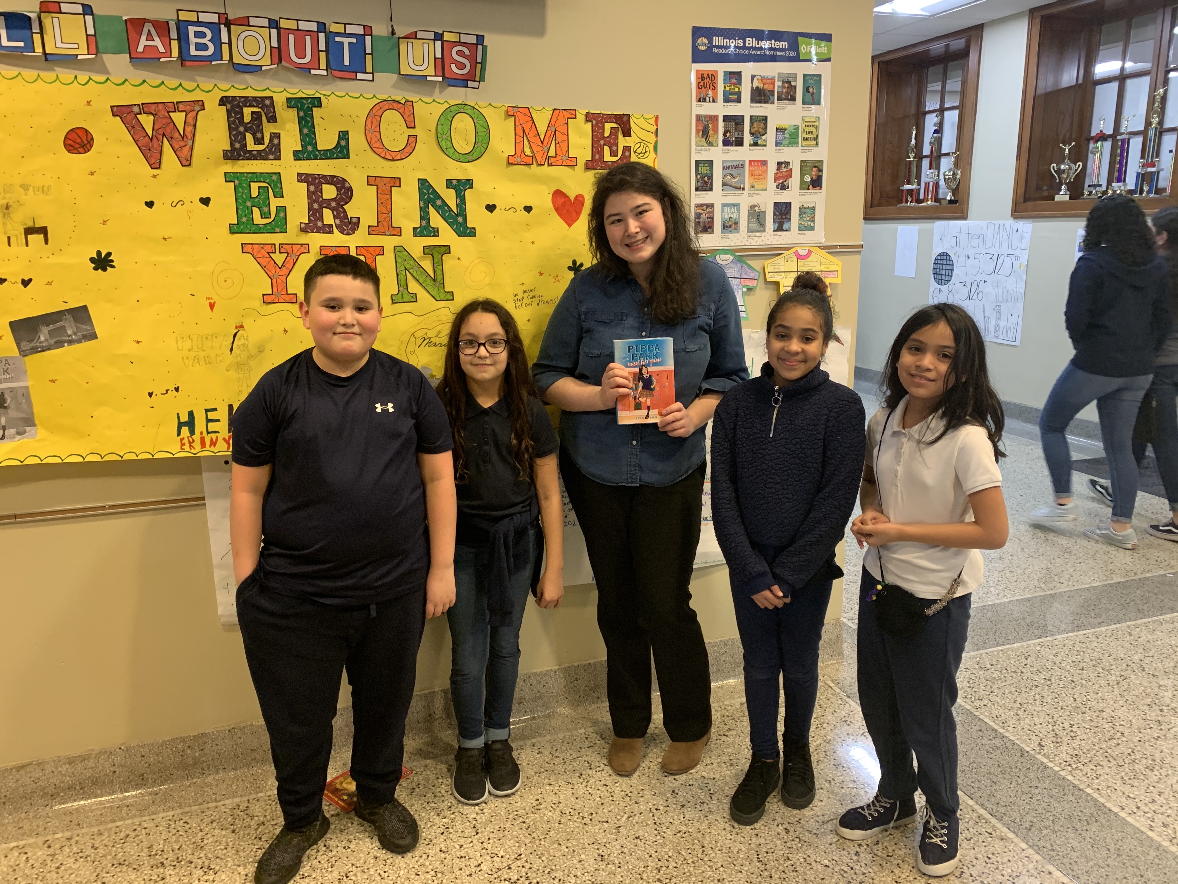 Author Erin Yun stands with students in a school hallway in front of a board that says welcome Erin Yun 